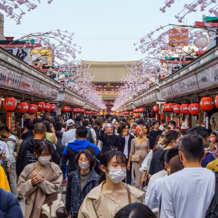 A crowded shopping street lined with red lanterns, leading to a temple gate