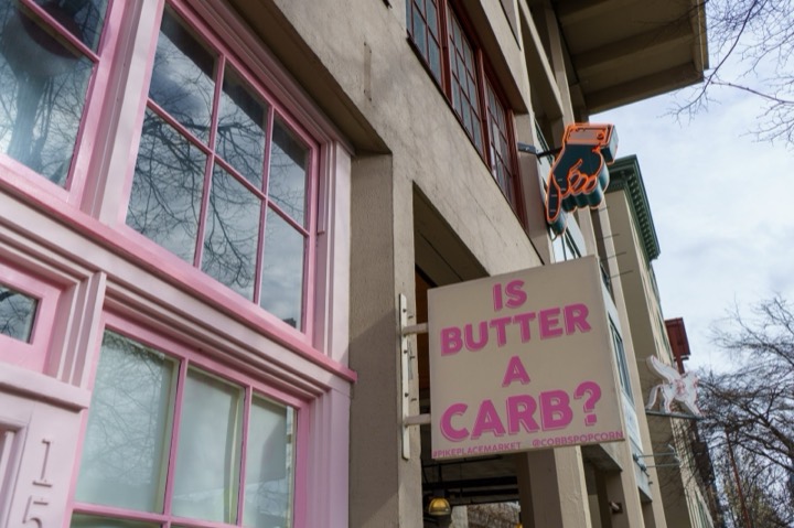 A pink-framed café window with a sign asking Is butter a carb?