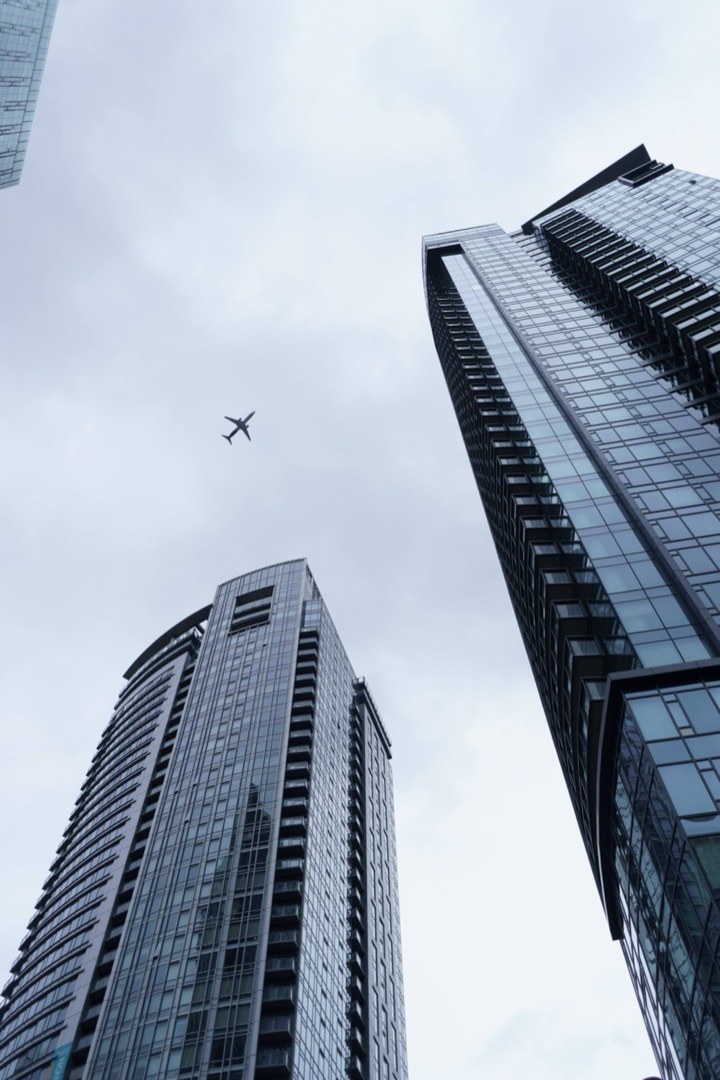 Two glass towers seen from below, with a plane overhead