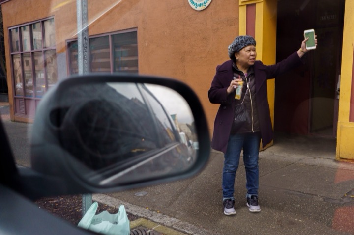 A woman holding up her phone in a doorway, framed by a car's side mirror