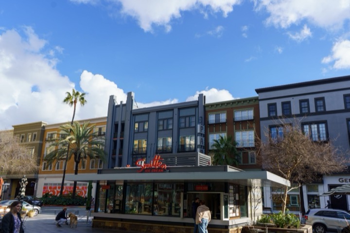 A shopping plaza with palm trees and a pavilion under a blue sky