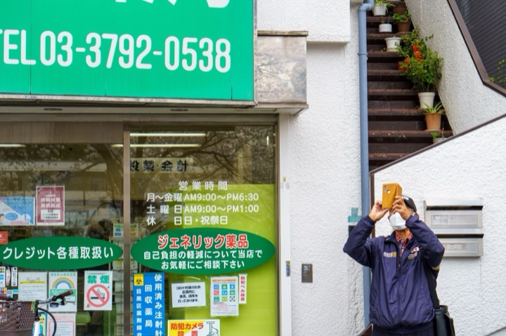 A man taking a photo outside a shop with green signs