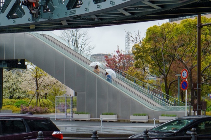 An escalator beneath an elevated track on a rainy day