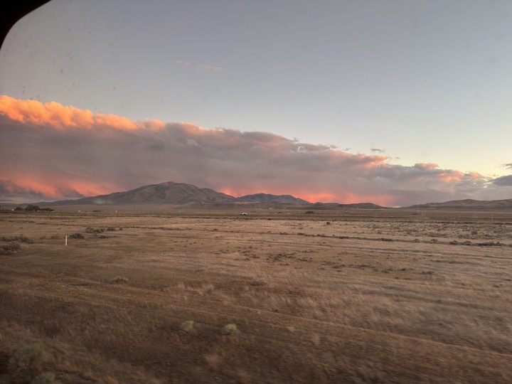 The sky turning pink over the desert at dusk, seen through the train window