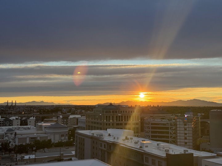 The sun setting over a city from a rooftop, a beam of light crossing the clouds