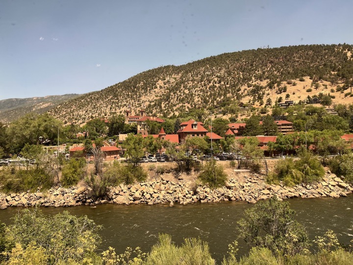 Red-roofed buildings by a river below dry hills, seen from the train