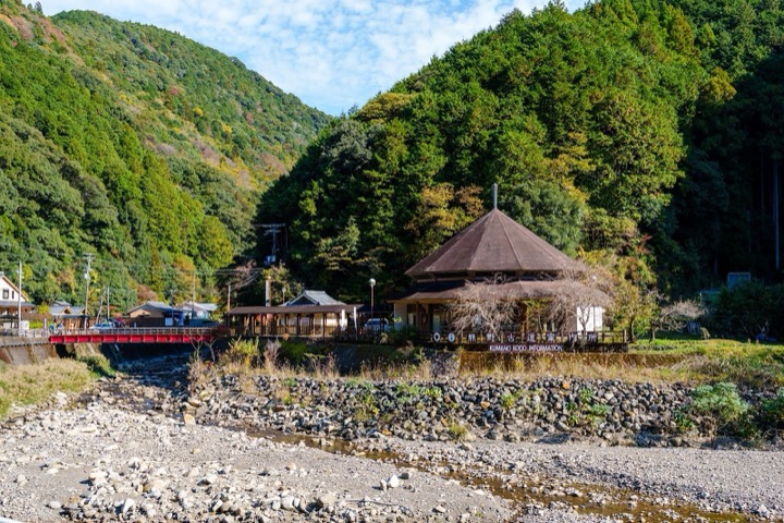 A thatched-roof house by a river in a wooded valley