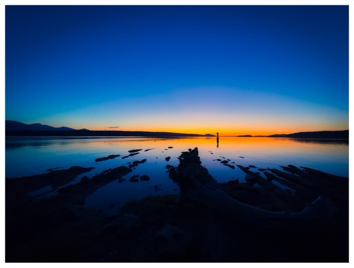 Sunset over still water, with rocks silhouetted in the foreground