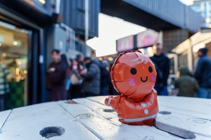 A gingerbread-man balloon on a table, with a crowd on the street behind