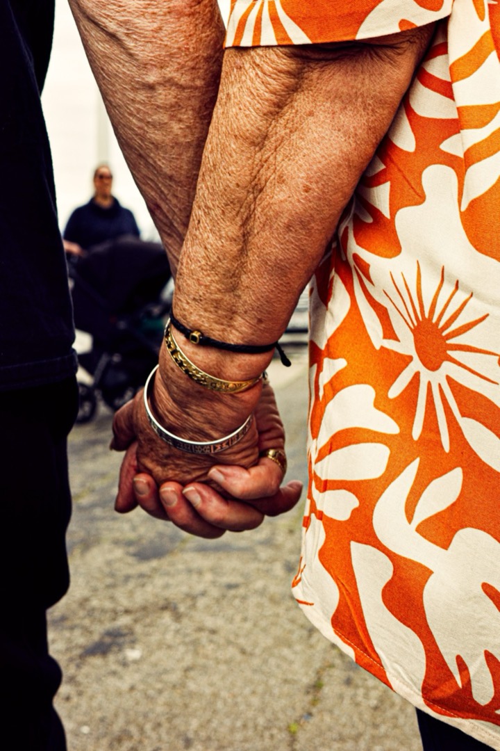 Close-up of two people holding hands, one in an orange floral dress
